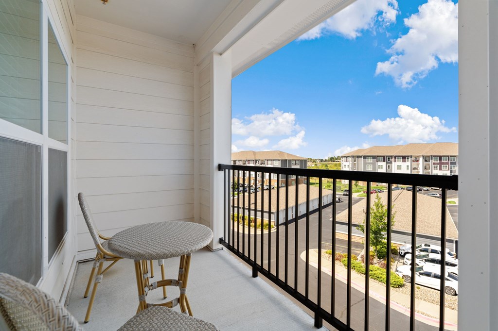 A balcony with a table and chairs overlooking a parking lot.