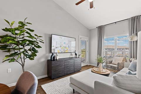 A living room with a grey couch, a brown chair, a wooden table, a potted plant, and a painting on the wall.