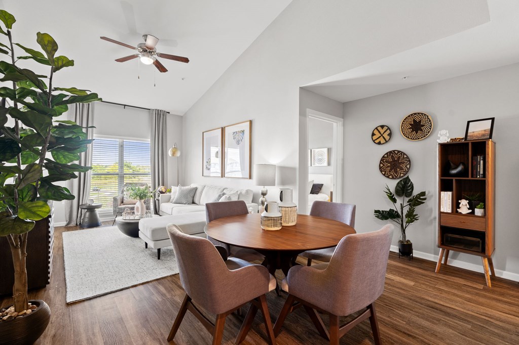 A dining room with a table set for two and a potted plant on the left.