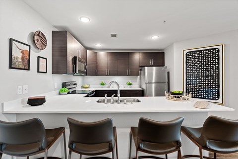 A modern kitchen with a white countertop and brown chairs.