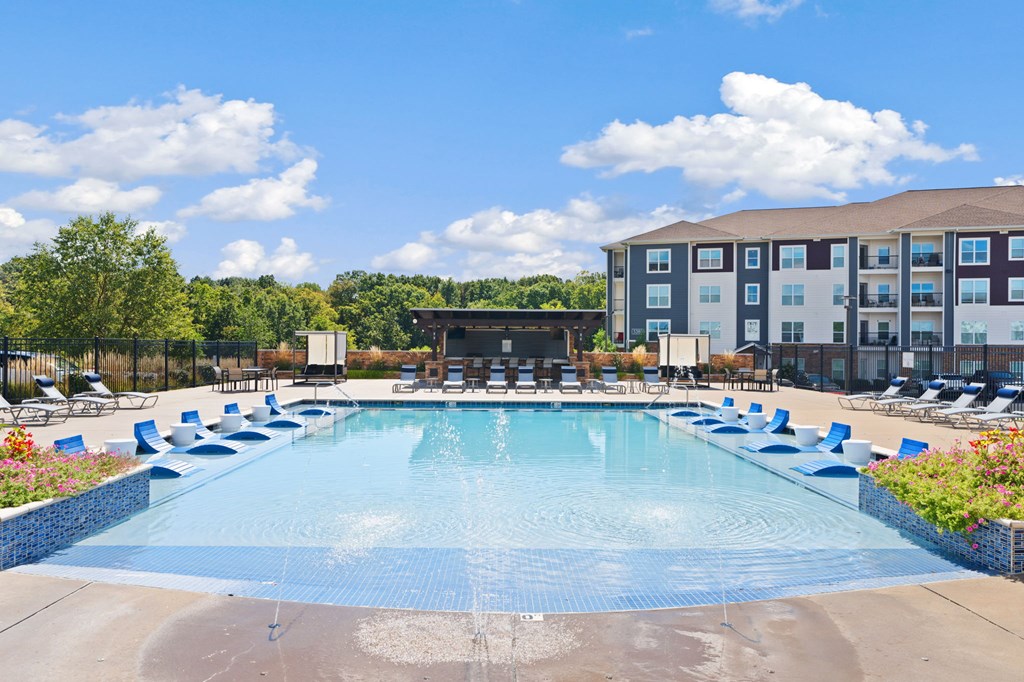 A large swimming pool surrounded by lounge chairs and a building in the background.