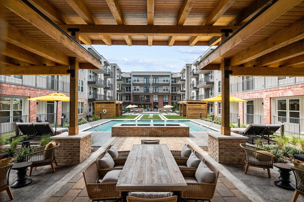 a patio with a wooden table and chairs and a pool in the background