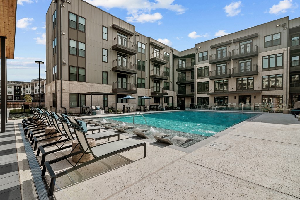 a swimming pool with chairs in front of an apartment building