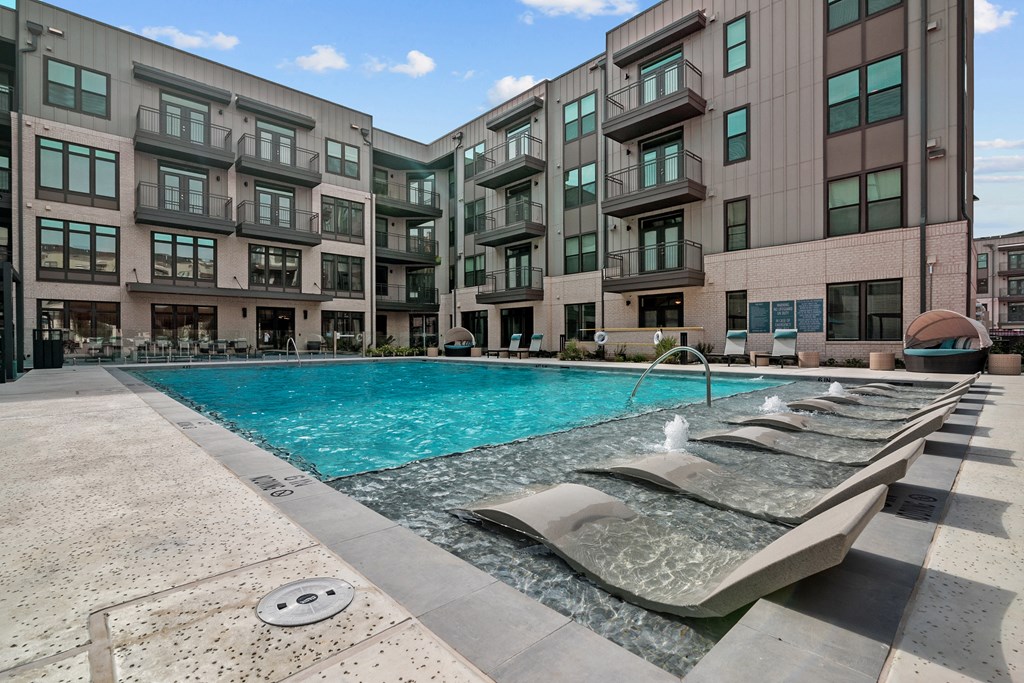a swimming pool with chaise lounge chairs next to an apartment building