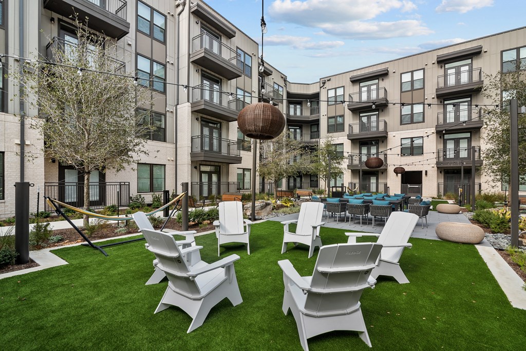 an outdoor lounge area with chairs and tables in front of an apartment building