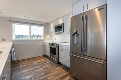 A modern kitchen with a stainless steel refrigerator and wooden flooring.