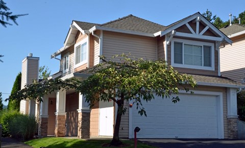 A house with a white garage door and a tree in front.