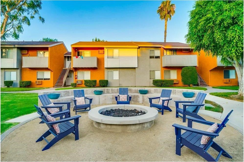A fire pit is surrounded by blue chairs in a courtyard.