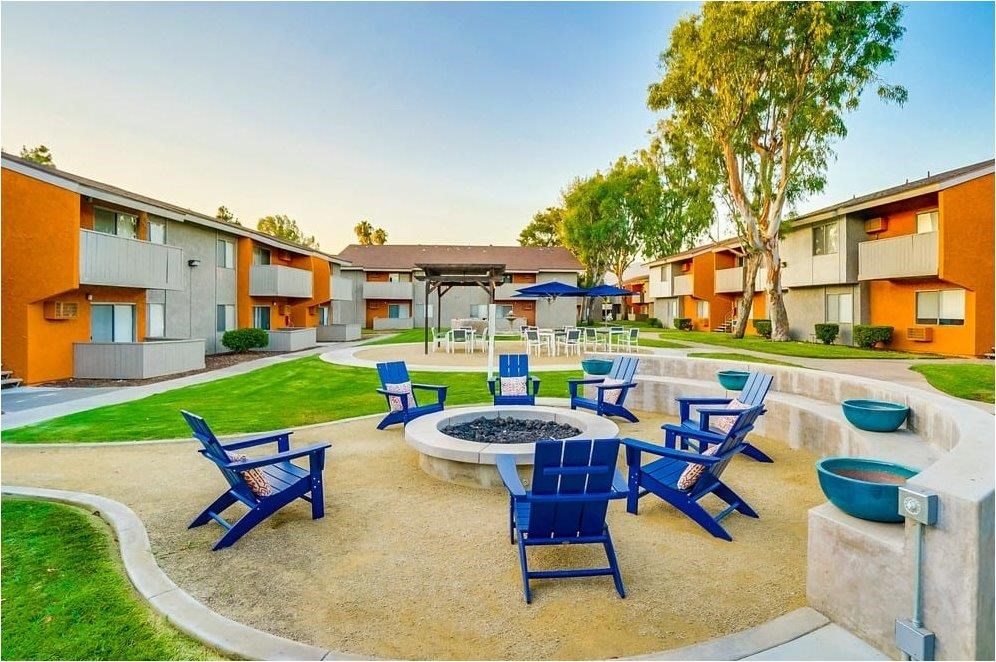 A sunny day at a residential complex with blue chairs and tables arranged around a fire pit.
