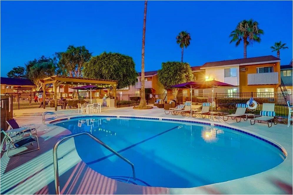 A swimming pool surrounded by lounge chairs and umbrellas at dusk.