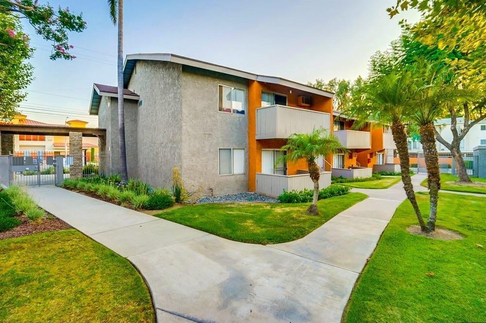 A modern apartment complex with a concrete walkway and palm trees.
