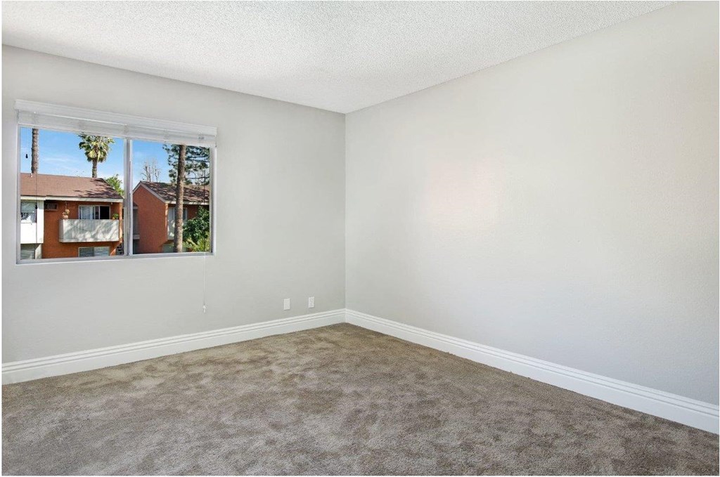 A room with a carpeted floor and a window showing a view of a house and trees outside.