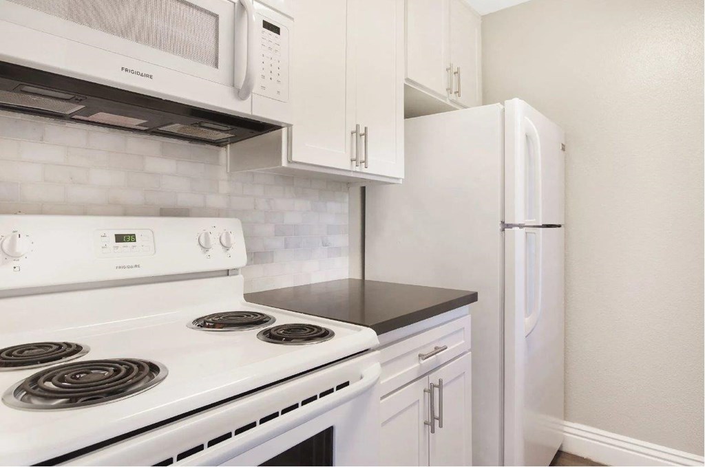 A white stove top oven with a white microwave above it and a white refrigerator to the right.