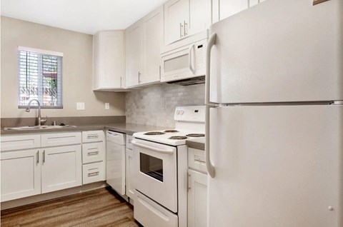 A white refrigerator stands in a kitchen with white cabinets and a white stove.