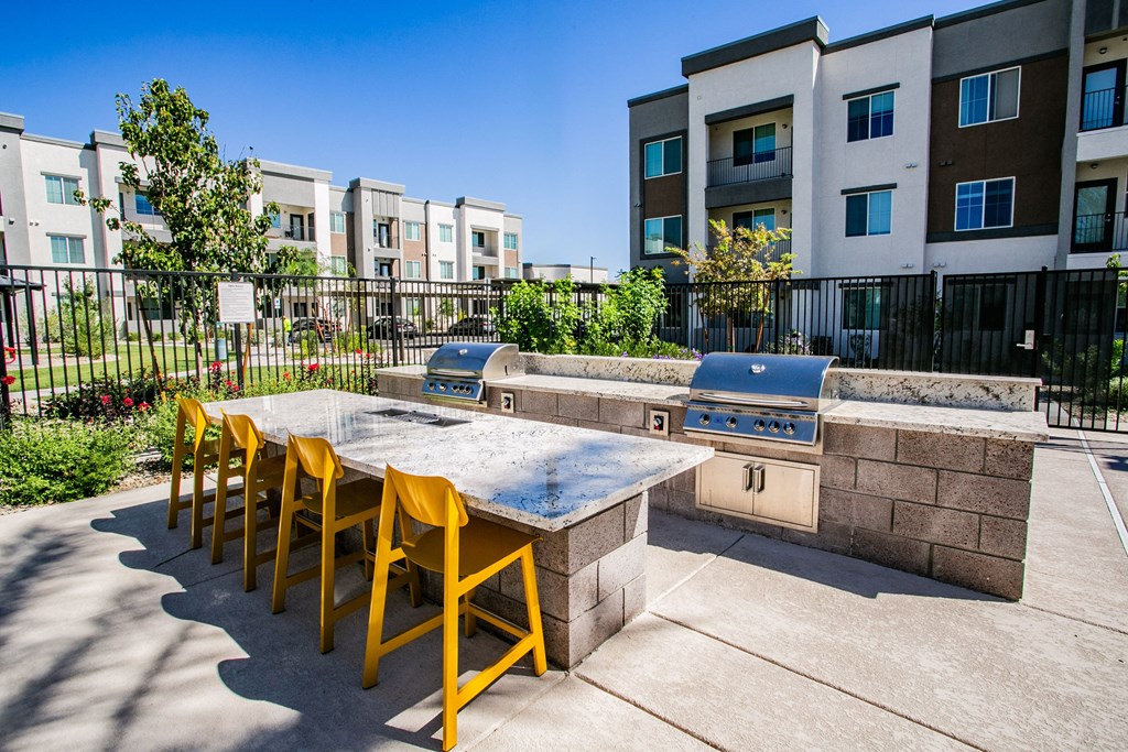an outdoor patio with a grill and a table with yellow chairs