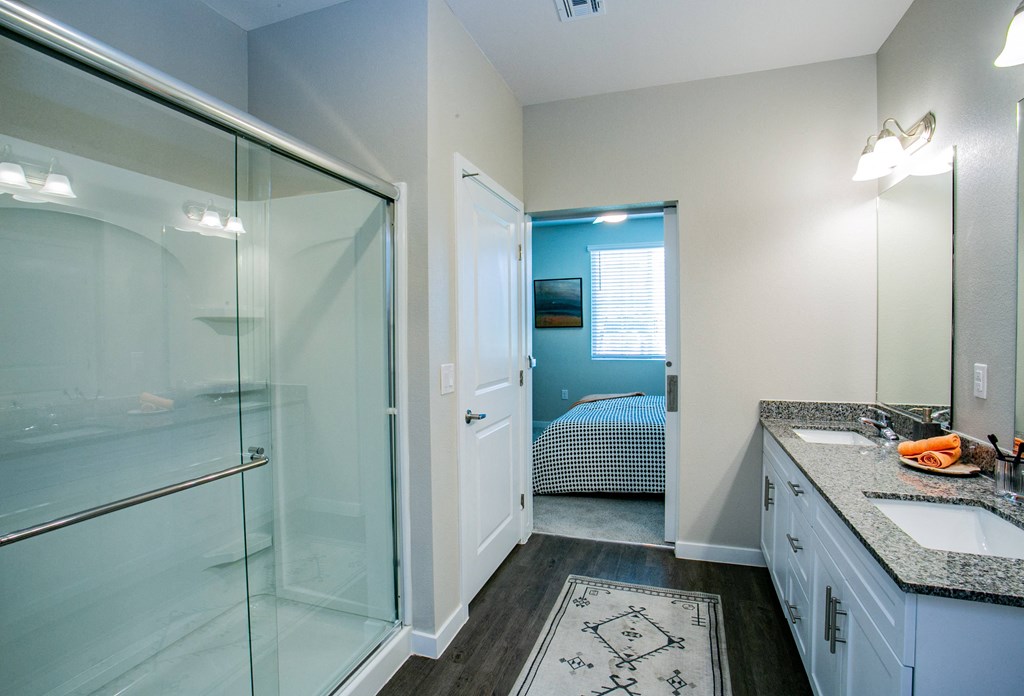 a bathroom with a glass shower and a sink and a bedroom