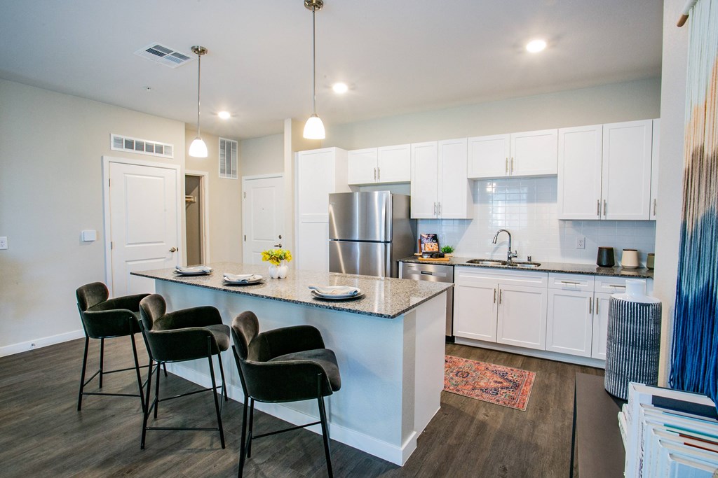 a kitchen with white cabinets and a blue island with black chairs