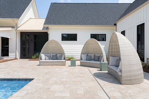 A white house with a pool and three wicker chairs.