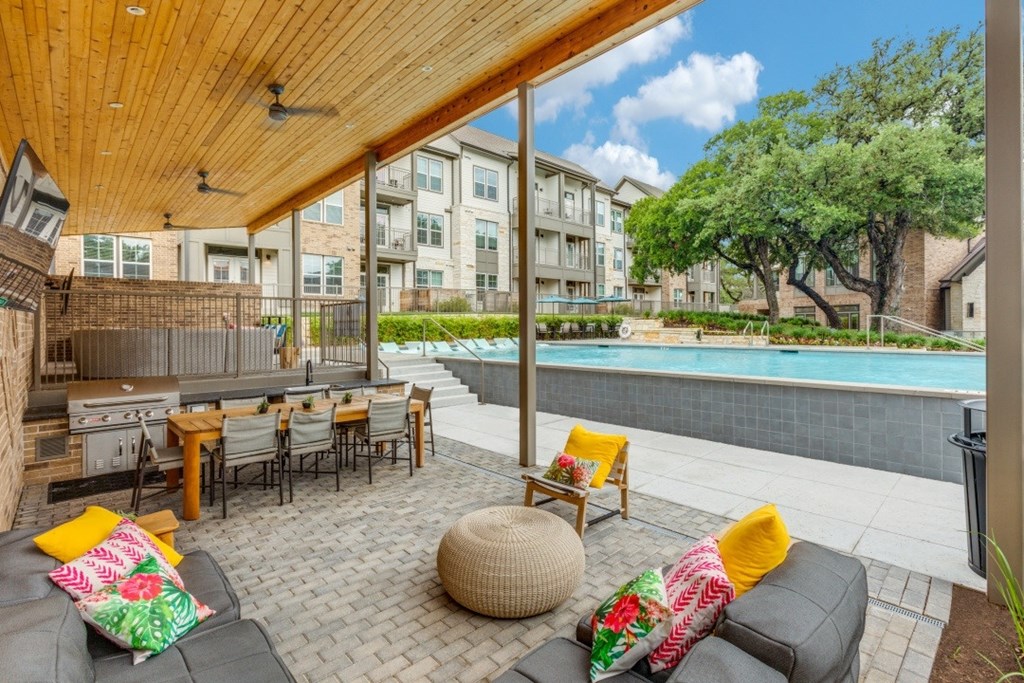 A patio with a table and chairs is surrounded by a pool and apartment buildings.