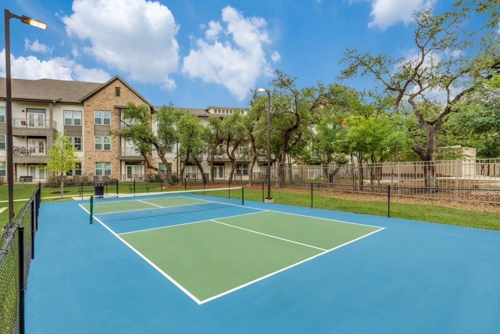 A tennis court is surrounded by a fence and trees.