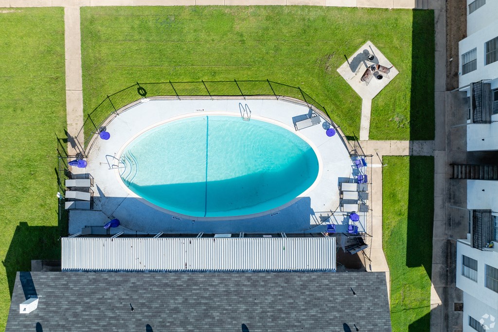 an aerial view of a swimming pool on a lawn with a building and a roof
