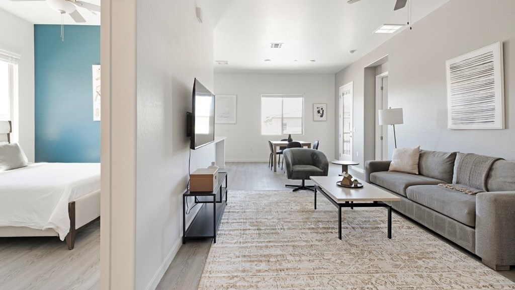A living room with a grey couch and a white bed.