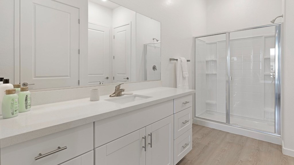 A white bathroom with a sink, mirror, and shower.