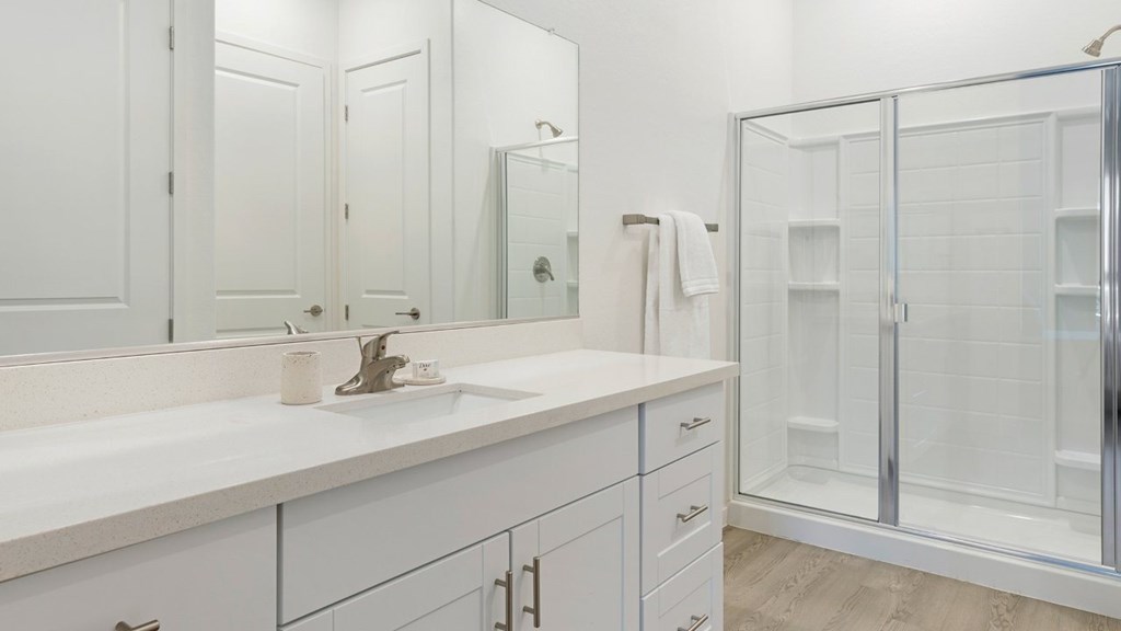 A white bathroom with a sink, mirror, and shower.