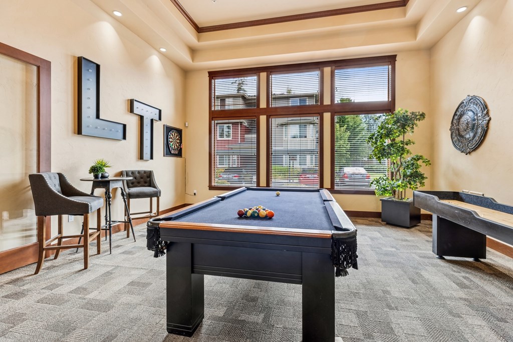 A pool table is in the middle of a room with a window and a plant.