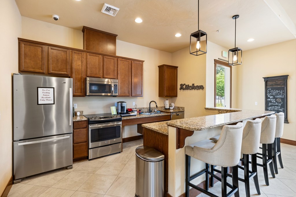 A kitchen with a refrigerator, microwave, oven, and bar stools.