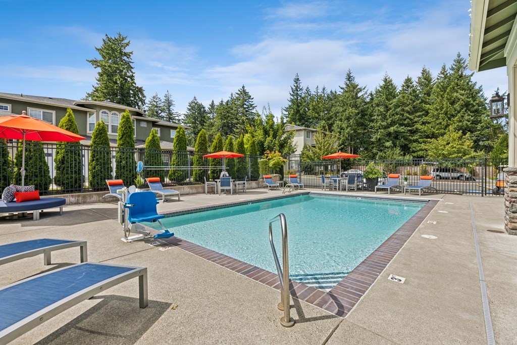 A pool with a red umbrella and blue chairs.