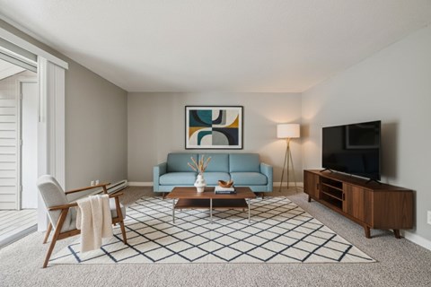 A living room with a blue couch, a coffee table, a chair, a painting, a lamp, and a television.