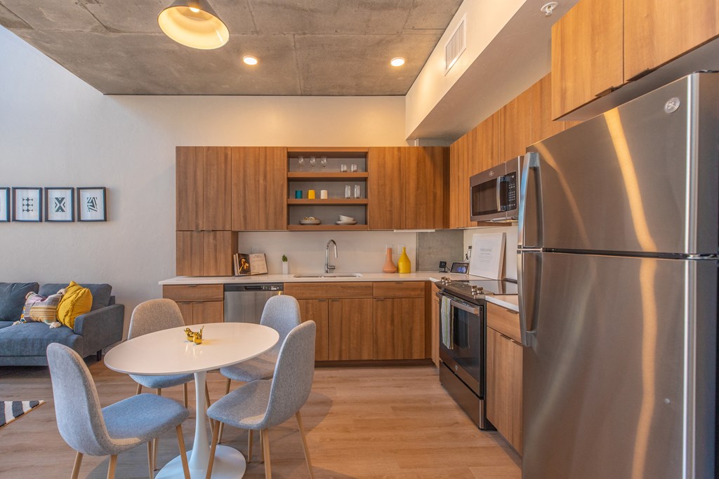 A modern kitchen with a stainless steel refrigerator, wooden cabinets, and a dining table with four chairs. at The Benedictine, Tucson, AZ