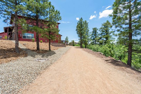 A red building is situated on a dirt road with trees on either side.