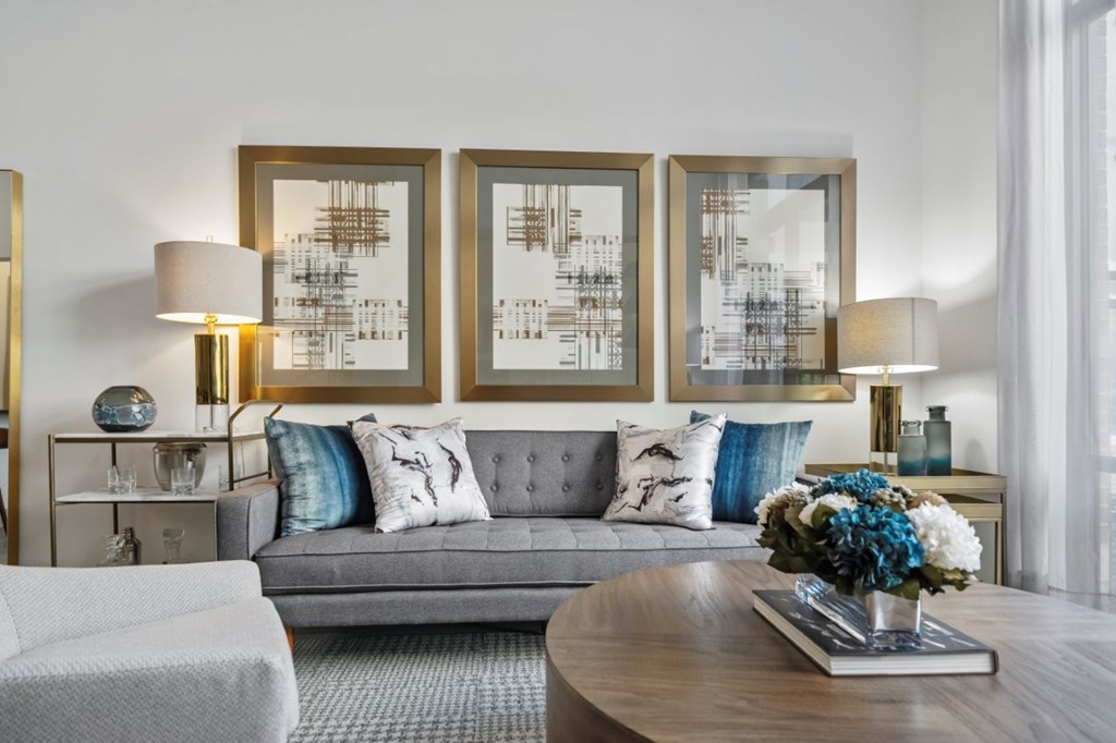 A modern living room with a grey sofa, a coffee table, and three framed artworks on the wall.