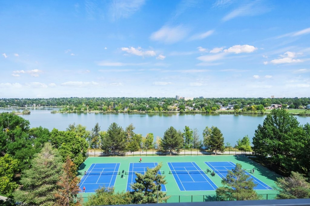 A tennis court surrounded by trees and a body of water.