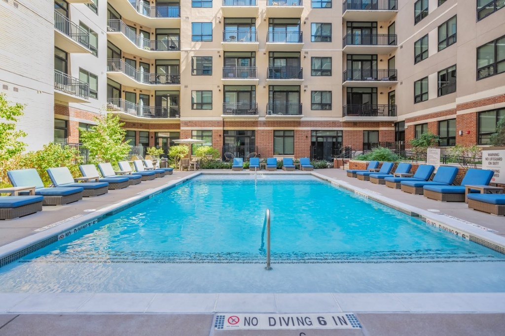 A large pool surrounded by lounge chairs and apartment buildings.