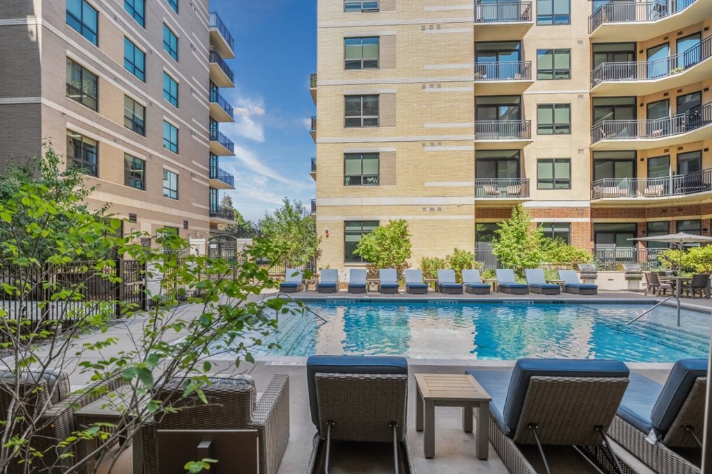 A pool surrounded by chairs and a building in the background.