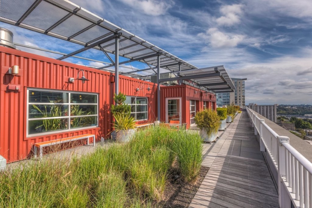 A series of red shipping containers are lined up on a wooden walkway with a metal roof above.