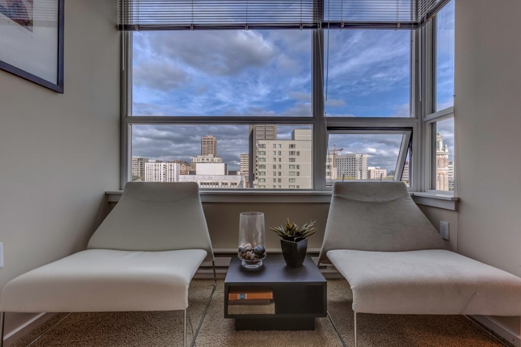 Two white chairs are placed in front of a window with a view of the city.