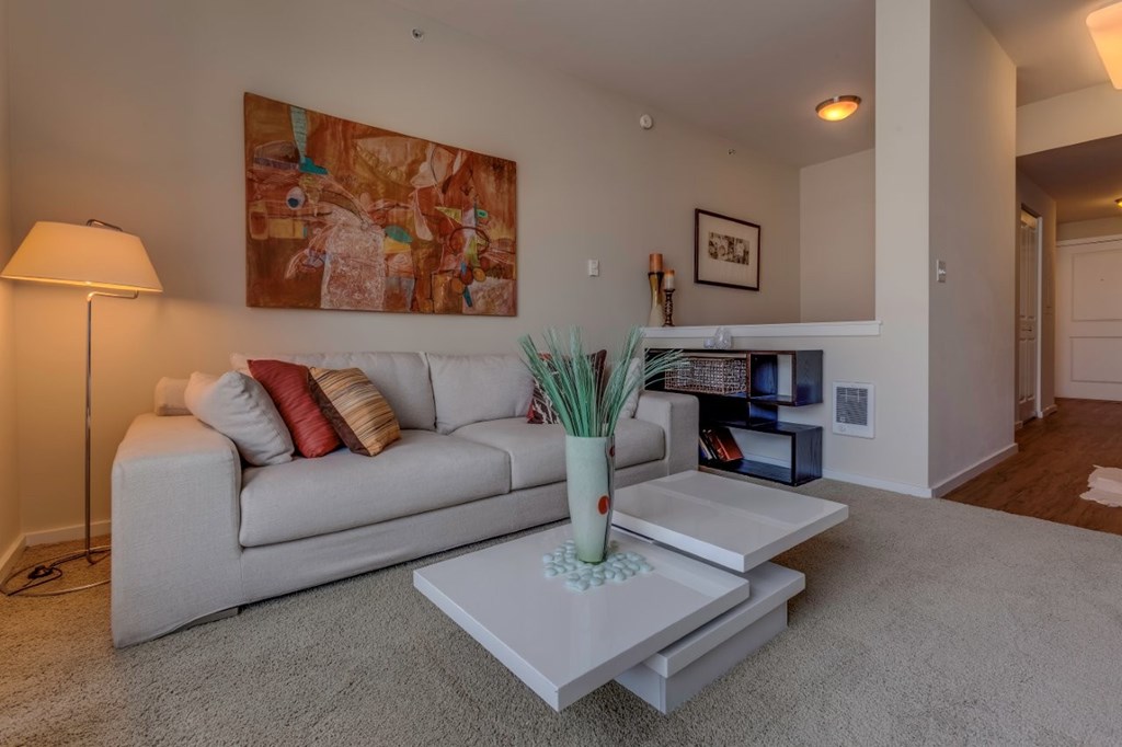 A living room with a grey couch, a white coffee table, and a painting on the wall.