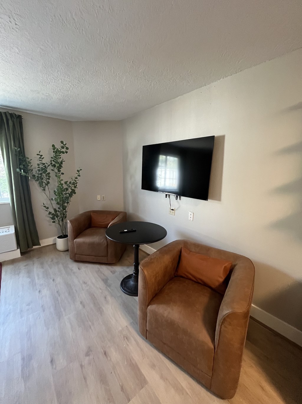 A living room with a brown couch, a small table, and a flat screen TV mounted on the wall.