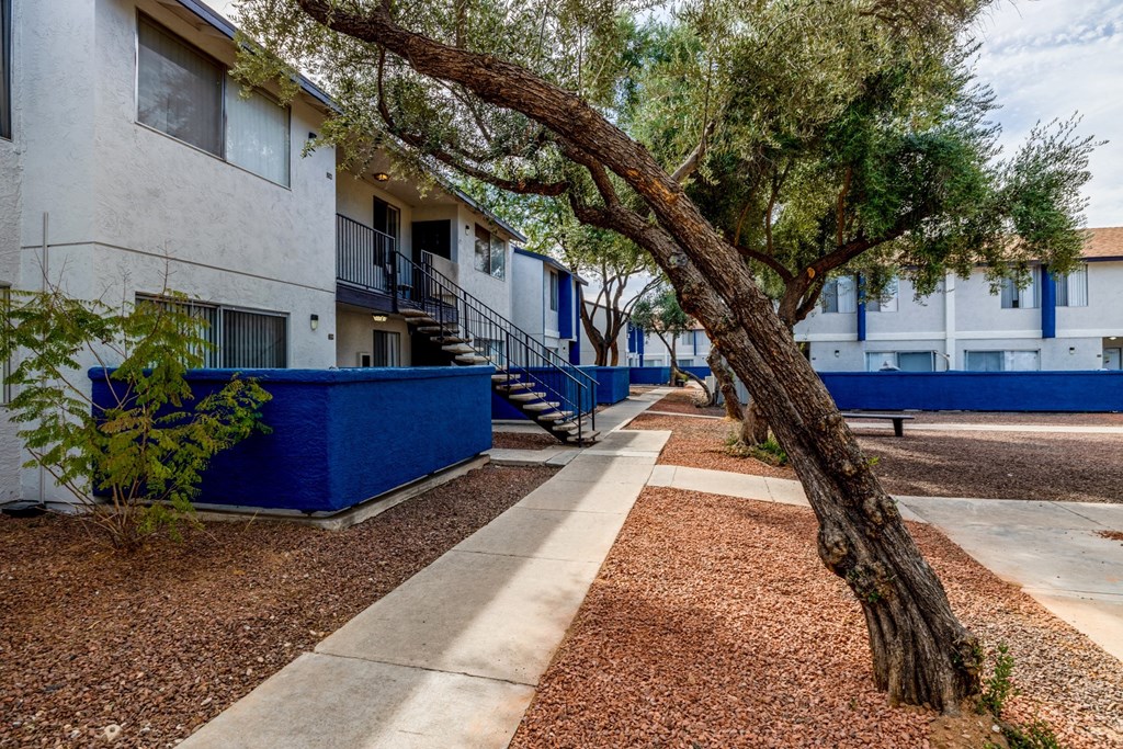 an apartment building with a sidewalk and trees in front of it