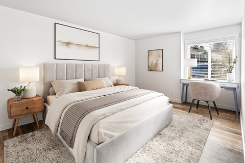 A bedroom with a large bed, a desk with a chair, and a window with blinds.