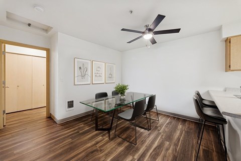 A room with a glass table and chairs, a ceiling fan, and a door.