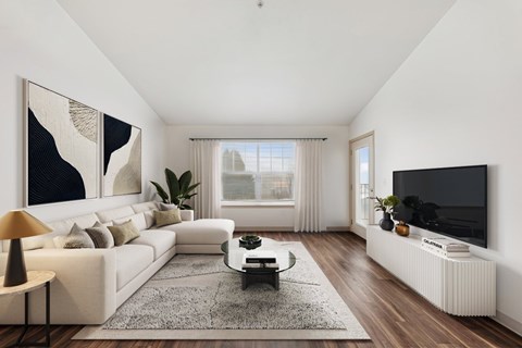 A modern living room with a white sofa, a coffee table, a large painting, a flat screen TV, and a window with curtains.