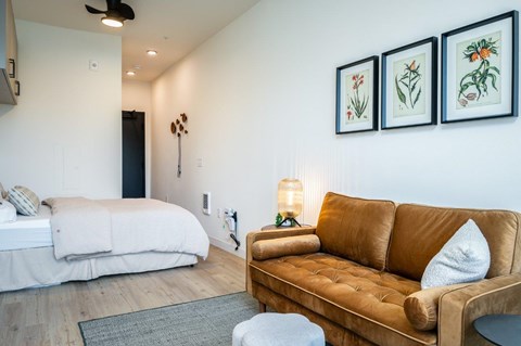 A brown couch sits in a living room with a white bed in the background.