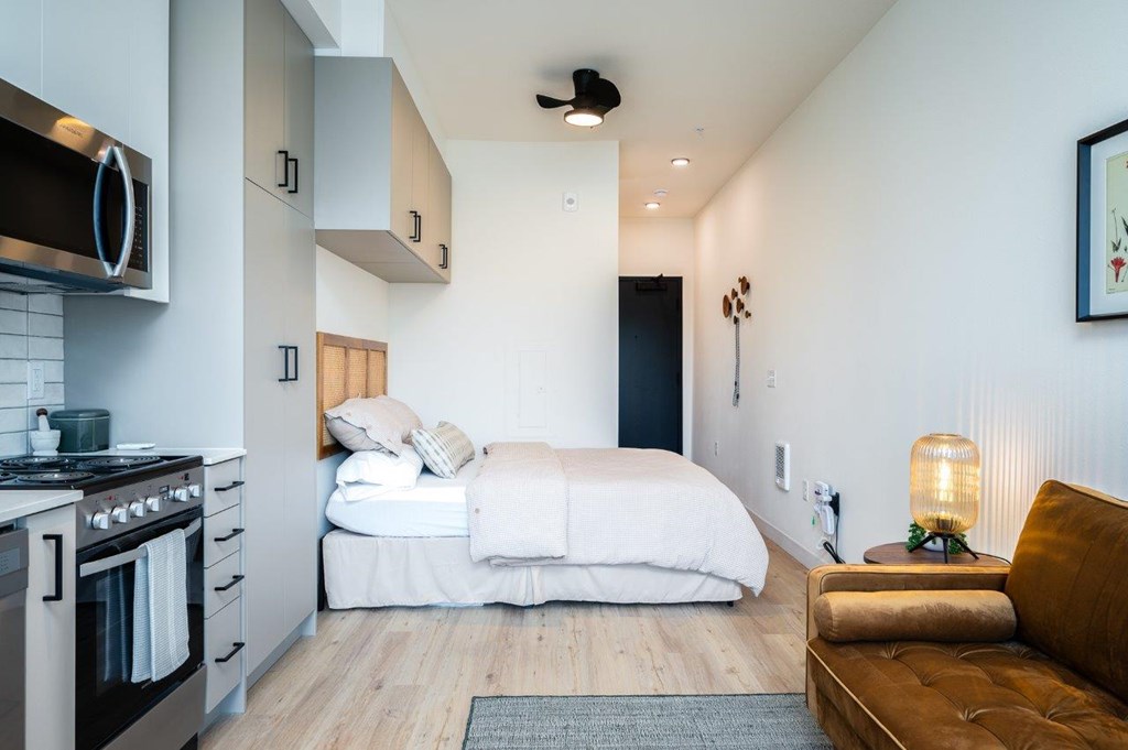 A modern Portland Oregon studio apartment bedroom with a bed, a couch, and a kitchen area.