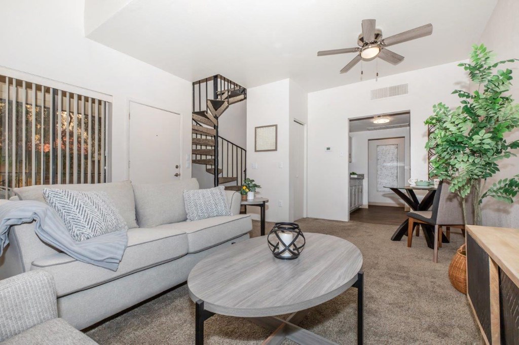 A living room with a grey couch, a round table, and a ceiling fan.