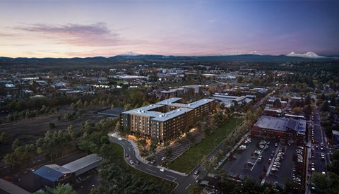 A modern building with a glass facade is the focal point of a cityscape at dusk.